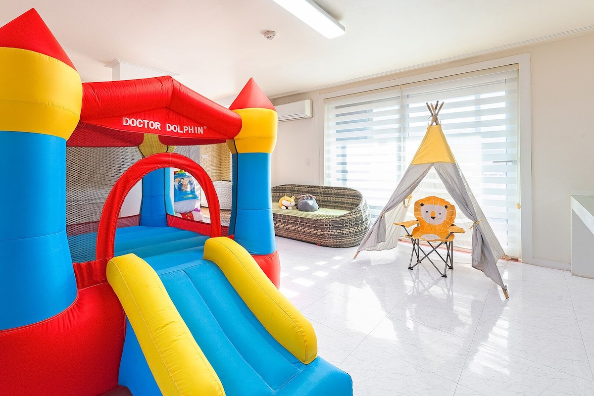 A colorful indoor play area with a bouncy castle, a slide, a teepee, and a play tent.