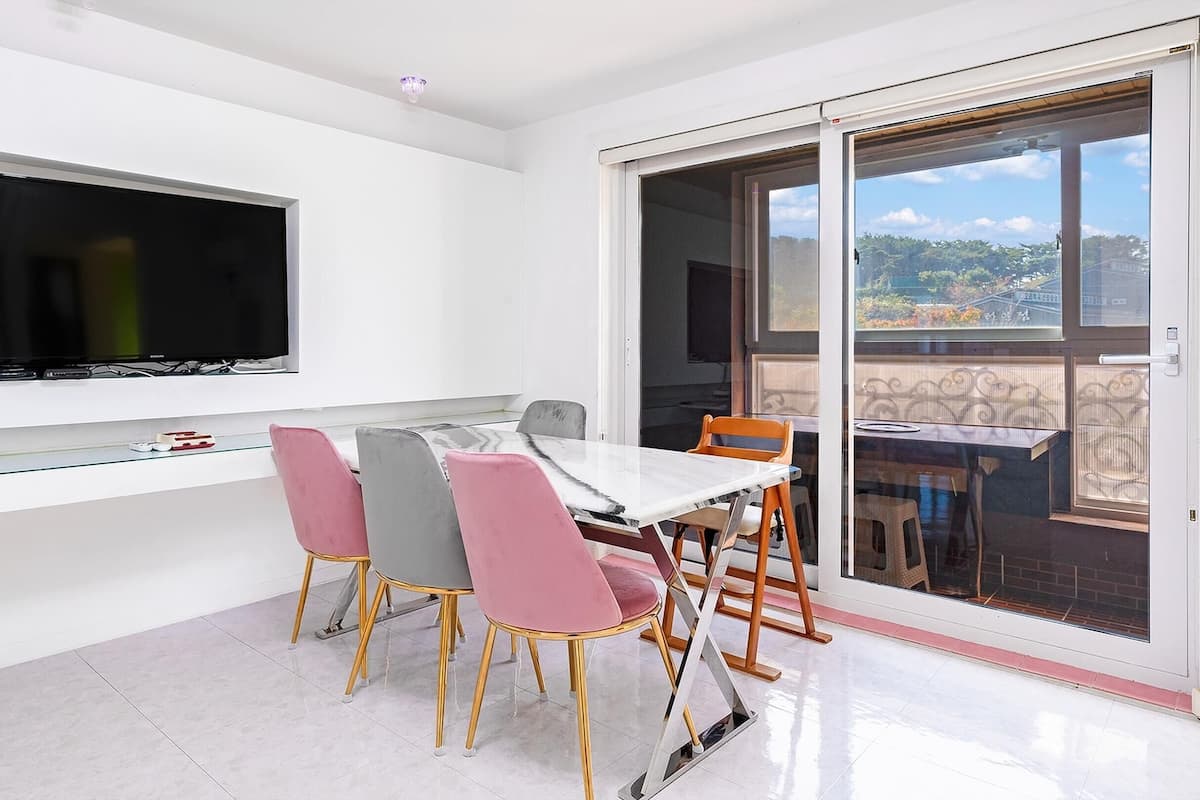 A modern dining area with a flat-screen TV, a glass-top table, and four chairs with gold legs.