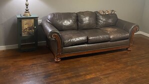 Ein Zimmer mit einem dunkelbraunen Ledersofa, einem kleinen Holztischchen mit einer Lampe und einem gerahmten Bild auf dem Tisch.