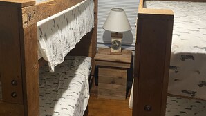 Ein kleiner, kompakter Raum mit zwei Holzbettklappen, einem kleinen Nachttisch mit Lampe und einem Fenster mit Jalousien.