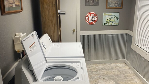 Ein Waschraum mit einer Waschmaschine und einem Trockner, einer Tür und einem Lüftungsgitter an der Decke.