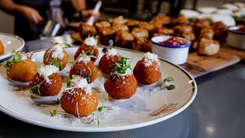 A plate of food with a variety of appetizers, including breaded balls garnished with cheese and greens, and a wooden board with more breaded items in the background.