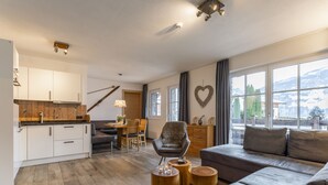 Ein modernes Wohnzimmer mit grauem Sofa, Holzboden und Bergblick durch große Fenster.