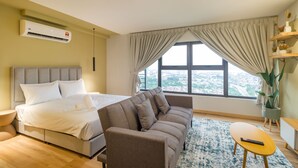 Ein modernes Hotelzimmer mit einem großen Bett, einer Couch, einem kleinen Tisch und Blick auf die Stadt durch das Fenster.