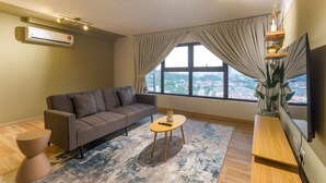 Ein modernes Wohnzimmer mit einem grauen Sofa, einem runden Couchtisch und einem großen Fenster mit Vorhängen.