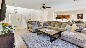 A spacious living room with a large sectional sofa, a coffee table, and a TV. A kitchen is visible in the background. - Pool, Game Room! Family-Friendly Surprise Retreat (Surprise)