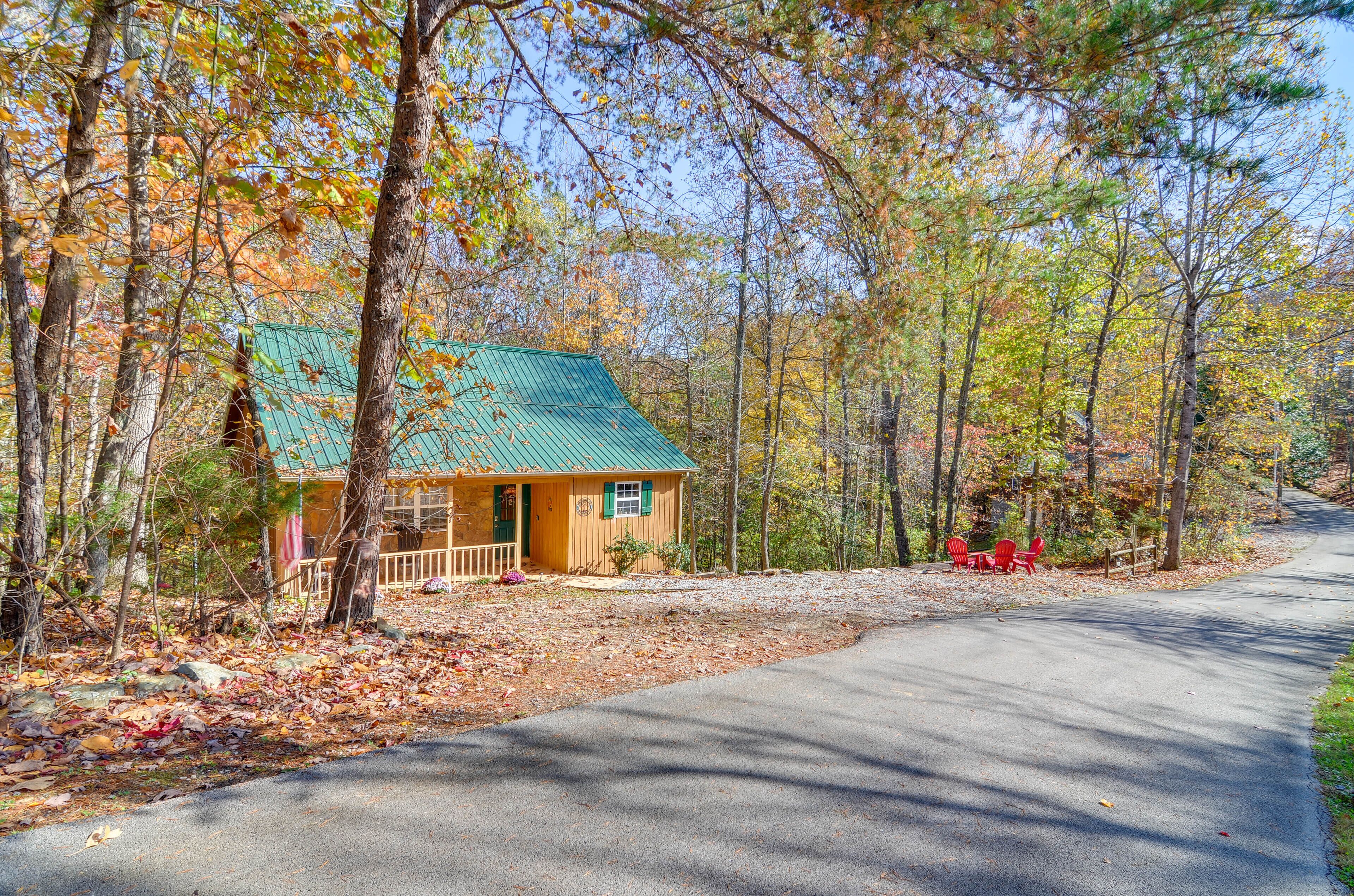 A cabin with a green roof, surrounded by trees and a paved road.