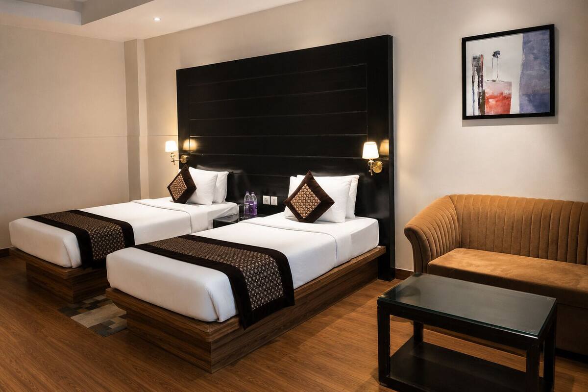 A hotel room with two beds, a sofa, a glass-top table, and a painting on the wall.