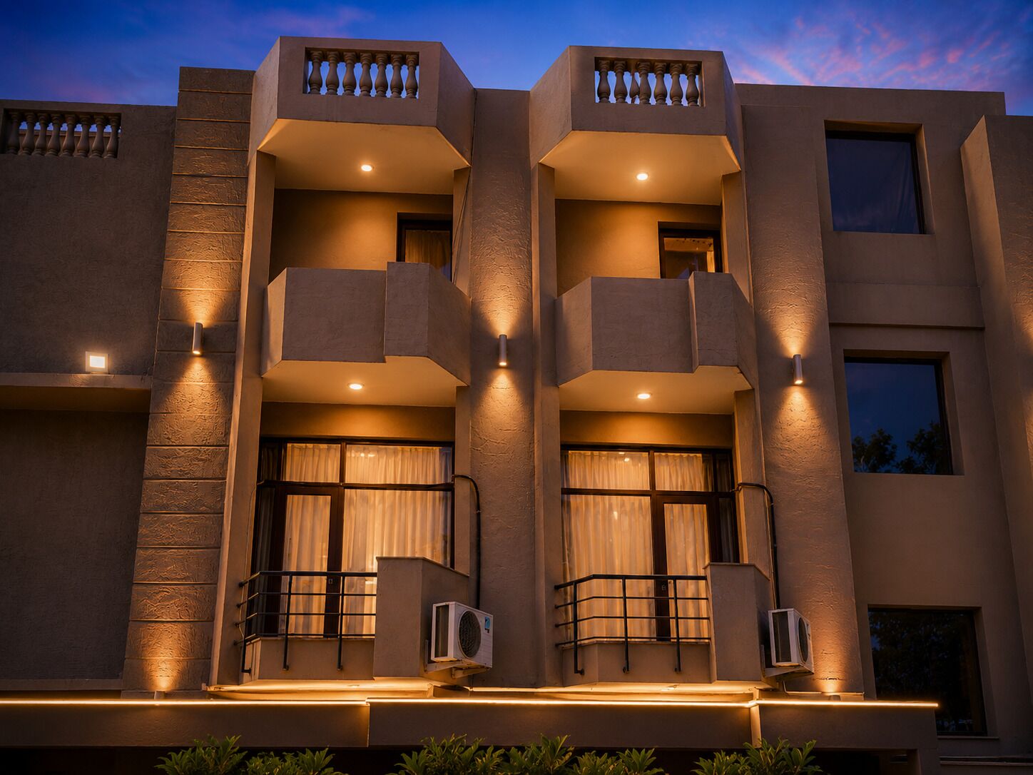 Un edificio de varios pisos con balcones, unidades de aire acondicionado e iluminación exterior cálida.