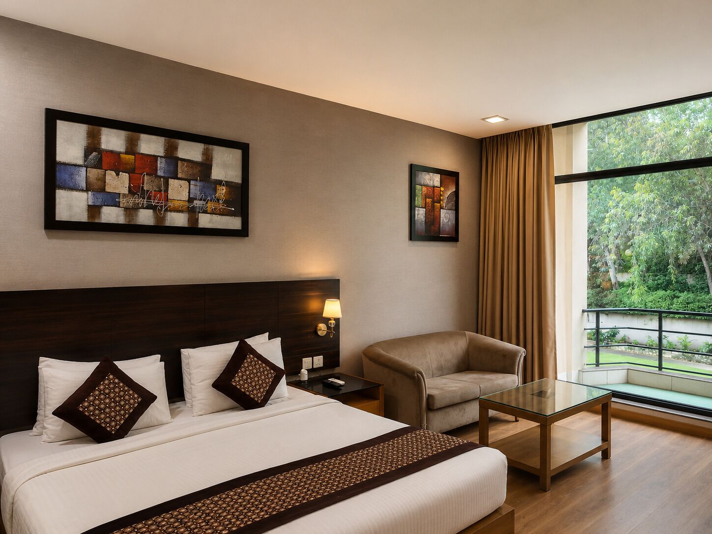 A hotel room with a bed, a chair, a small table, and two artworks on the wall.