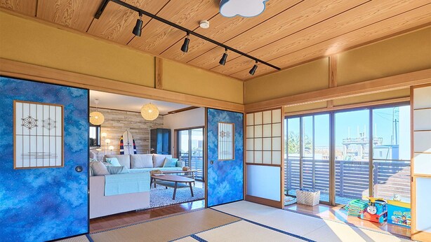 Une pièce de style japonais traditionnel, avec un sol recouvert de tatamis, des portes coulissantes et une vue sur l’extérieur.