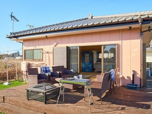 Een huis met een terras, voorzien van rieten meubels, een tafel en een barbecue.