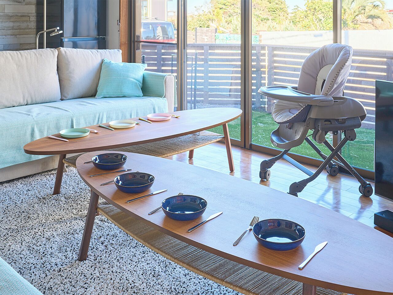 Un coin repas avec une table en bois dressée pour quatre personnes, un canapé et un transat pour bébé.