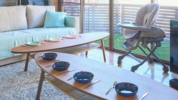 Un coin repas avec une table en bois dressée pour quatre personnes, un canapé et un transat pour bébé.