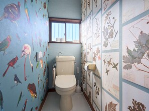 Een badkamer met toilet, raam en muren versierd met planten en vogels.