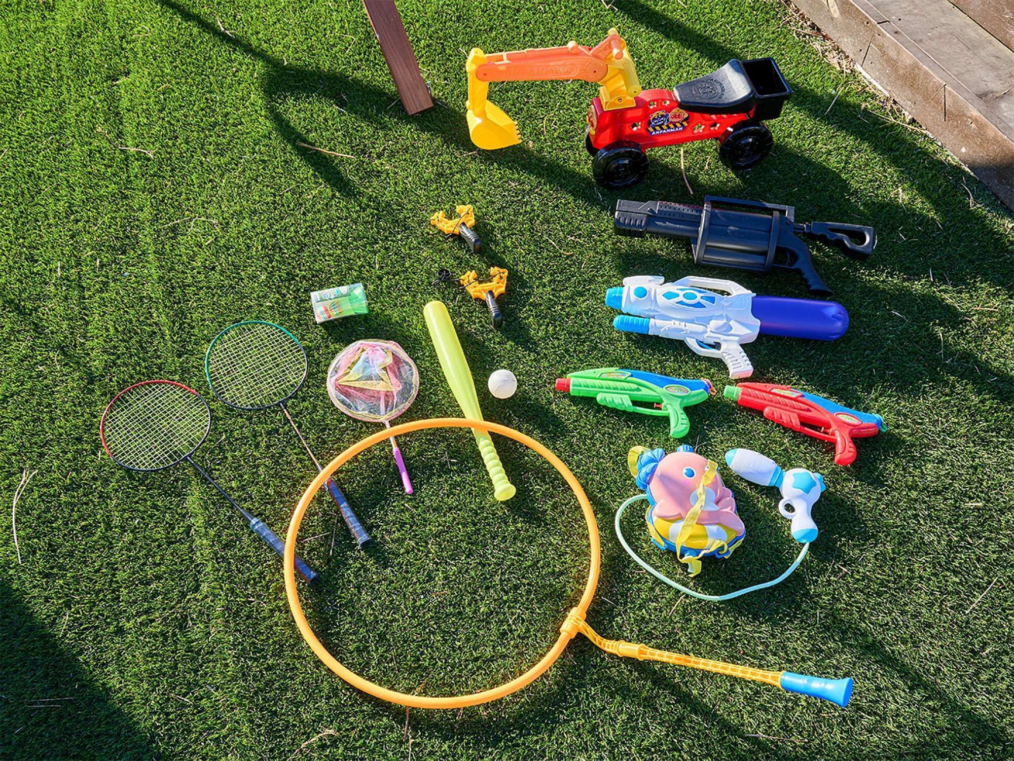 A variety of children's toys and sports equipment laid out on a grassy surface.