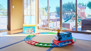 Une pièce dotée de grandes fenêtres, d’un espace de jeux avec un train jouet et d’un tapis de jeu à l’effigie de « Pat’ Patrouille ».