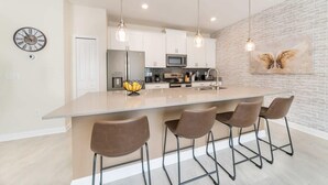 Una cocina moderna con una isla central, luces colgantes y un reloj en la pared.