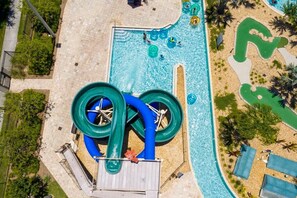 An aerial view of a water park with a large water slide, a swimming pool, and a sandy area with lounge chairs. - Beautiful house, great location, private pool (Kissimmee)