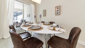 Comedor con una mesa redonda, sillas marrones y mantel blanco.