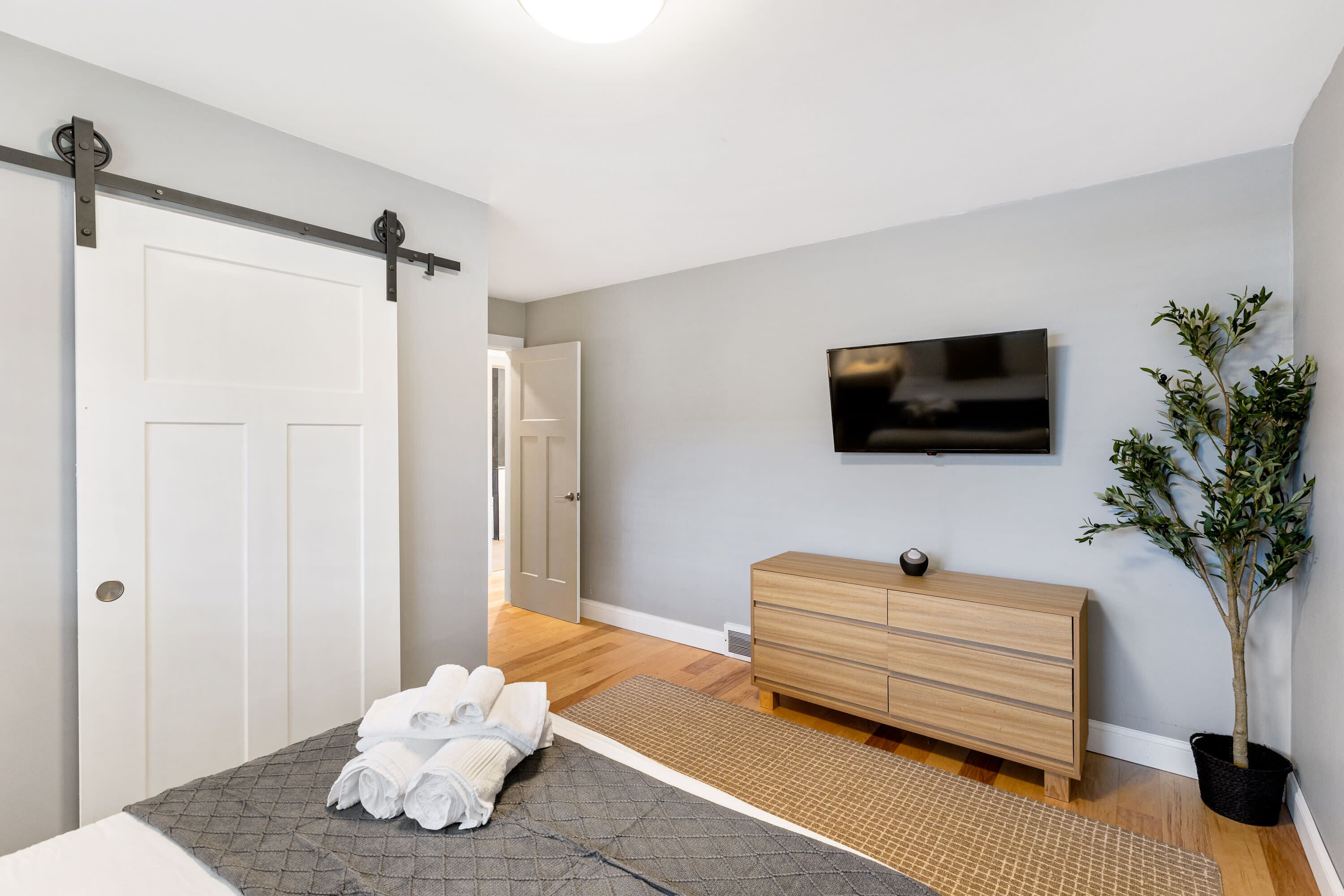 Ein Schlafzimmer mit Bett, Kommode, Fernseher und einer Topfpflanze.