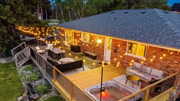 Un giardino con una vasca idromassaggio, un patio in legno, posti a sedere all'aperto e luci decorative.