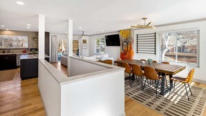 Una cucina moderna con isola centrale, zona pranzo con tavolo e sedie in legno, e un'ampia finestra con tende.