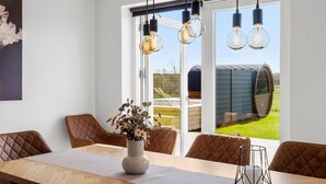 Comedor con mesa de madera, sillas acolchadas, lámparas colgantes y vistas a una bodega a través de puertas de cristal.