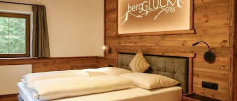 A wooden-paneled bedroom with a bed, a nightstand, a wall-mounted lamp, and a window with curtains.
