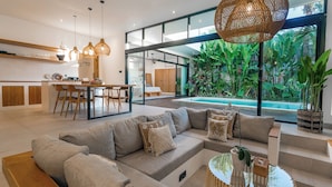 Um espaço de estar moderno com sofá, área de jantar, cozinha e vista para uma piscina e jardim.