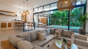 Un espacio habitable moderno con sofá, zona de comedor, cocina y vistas a una piscina y jardín.