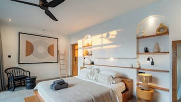 A modern bedroom with a bed, a ceiling fan, a framed artwork, a wooden ladder, and a bedside table with decorative items.