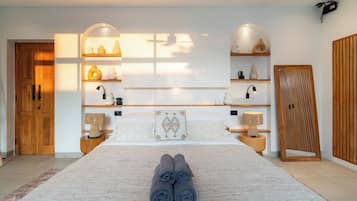 Un dormitorio moderno con una cama grande, dos mesitas de noche con lámparas, un armario y estantes con objetos decorativos.