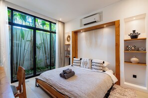 A bedroom with a large window, a bed with rolled towels, and a wall-mounted air conditioner. - Jardin Villa by Betterplace (Pecatu)