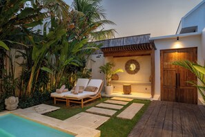 A pool area with lounge chairs, a wooden deck, and a stone pathway leading to a door. - Jardin Villa by Betterplace (Pecatu)