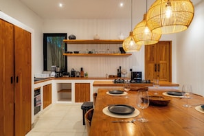 A modern kitchen with wooden cabinets, a dining table set for four, and a hanging light fixture. - Jardin Villa by Betterplace (Pecatu)