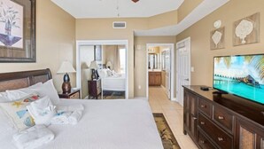 A hotel room with a bed, a television, a ceiling fan, and a view of the ocean. - Seychelles 101 (Panama City Beach)