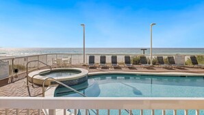 A pool area with a view of the ocean, a hot tub, and lounge chairs. - Seychelles 101 (Panama City Beach)