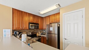A modern kitchen with wooden cabinets, stainless steel appliances, and a welcome sign. - Seychelles 205 (Panama City Beach)