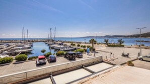 Un port de plaisance avec des bateaux amarrés, un espace de stationnement et une vue sur la mer et les collines lointaines.