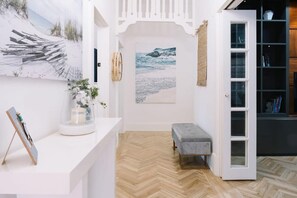 Ein Zimmer mit Fischgrätparkett, einer Bank, einer weißen Tür und einem Bücherregal.