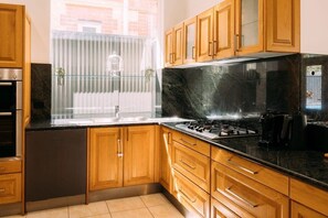 Una cocina con armarios de madera, encimera negra, lavavajillas de acero inoxidable y estufa a gas.