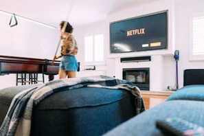 Ein Wohnzimmer mit einem Fernseher, der 'NETFLIX' anzeigt, einem Klavier und einer Person, die fegt.