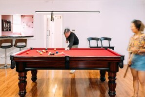 Une table de billard dans une pièce au plancher en bois, avec un bar en arrière-plan.