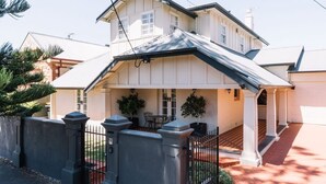 A two-story house with a covered porch, a gated entrance, and a brick pathway leading to the front door. - Glenelg 4BR with pool, 2 min to beach, sleeps 13 (Glenelg South)