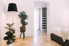 A modern bedroom with a bed, a floor lamp, and two potted plants.