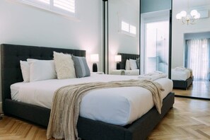 Une chambre à coucher moderne avec un grand lit, une tête de lit sombre et un miroir qui reflète la pièce.