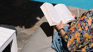 A person reading a book by a pool with a white table and a grey bench. - Glenelg 4BR with pool, 2 min to beach, sleeps 13 (Glenelg South)