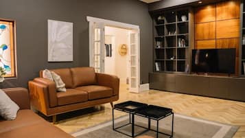 A modern living room with a brown leather sofa, a black coffee table, a television, and a bookshelf.