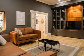 Un salon moderne avec un canapé en cuir marron, une table basse noire, un téléviseur et une bibliothèque.